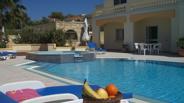 Una piscina con sillones de descanso y una cesta de frutas.