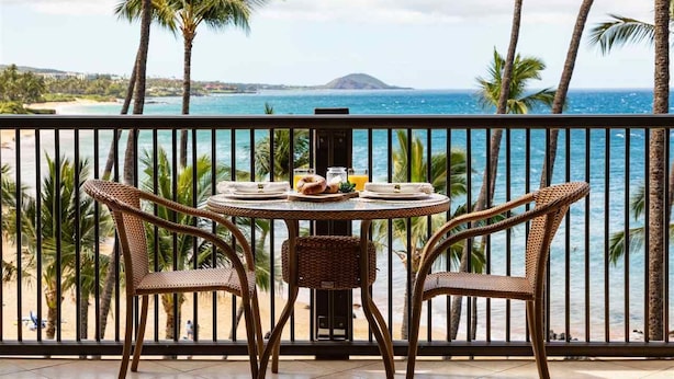 A balcony with wicker chairs and a round table set for breakfast, overlooking a beach and ocean. - Mana Kai 404, Beautifully Renovated, Unbelievable Ocean View (Kihei)