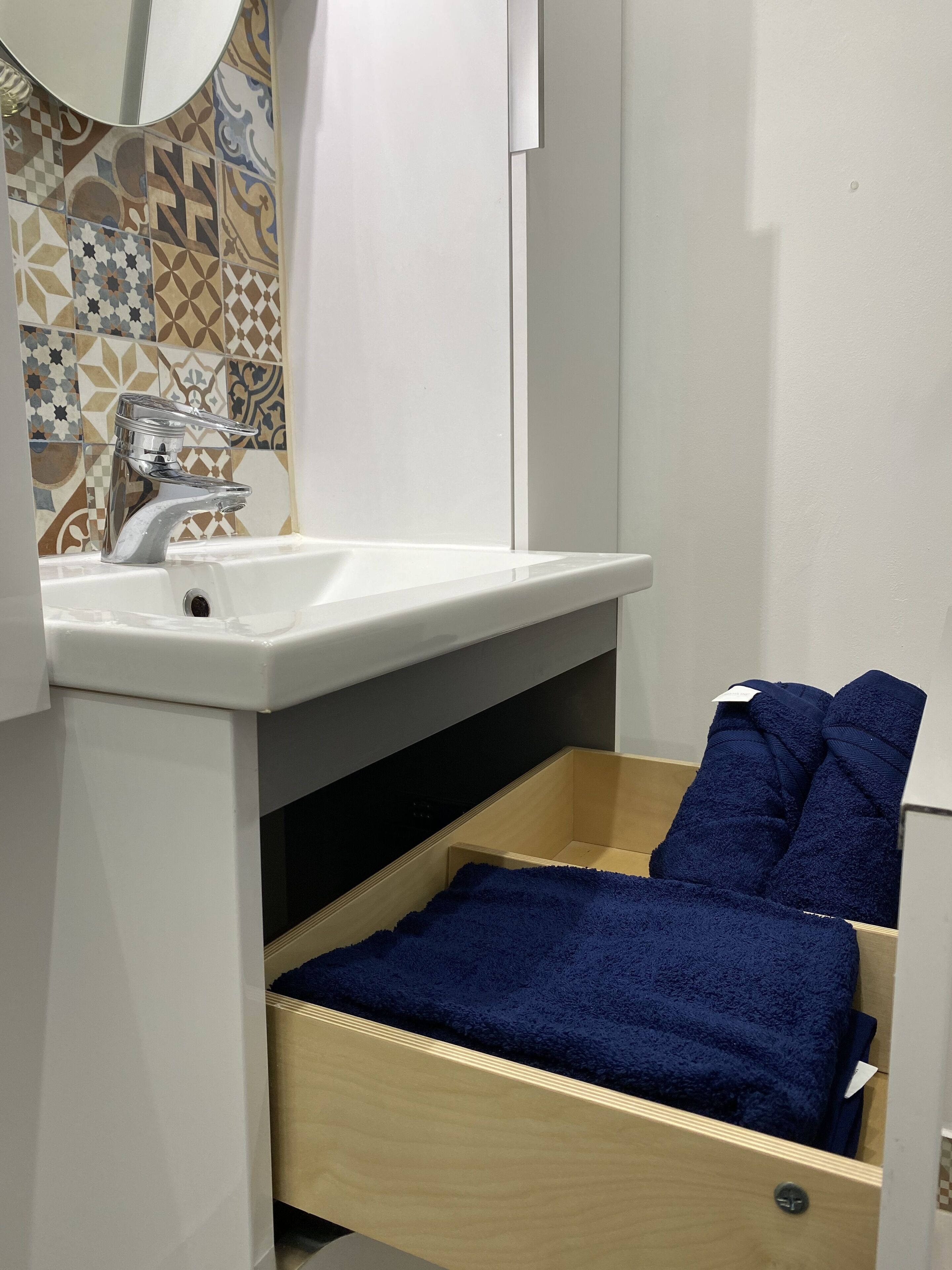 A bathroom with a white sink, a mirror, and a wooden drawer with a blue towel.