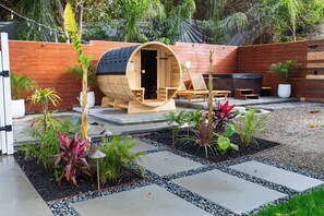 A wooden sauna with a bench and a small table, surrounded by potted plants and a gravel path. - 3bd/2.5bath house+Ocean Views,Spa, Sauna,Fire Pit & Huge backyard (San Juan Capistrano)