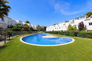 A swimming pool surrounded by well-maintained grass, with white buildings in the background.
