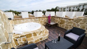 Een terras op het dak, met een stenen muur, een hottub, rieten meubels en een tafel met wijnglazen.