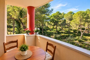 A balcony with a wooden table and chairs, a red pillar, and potted plants.