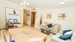 A living room with a wooden dining table, chairs, a sofa, and a television.