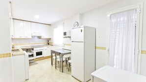 A compact kitchen with white cabinets, a dining table with four chairs, a refrigerator, and a microwave.