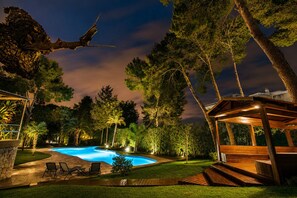 Une piscine entourée d’arbres et un kiosque en bois.