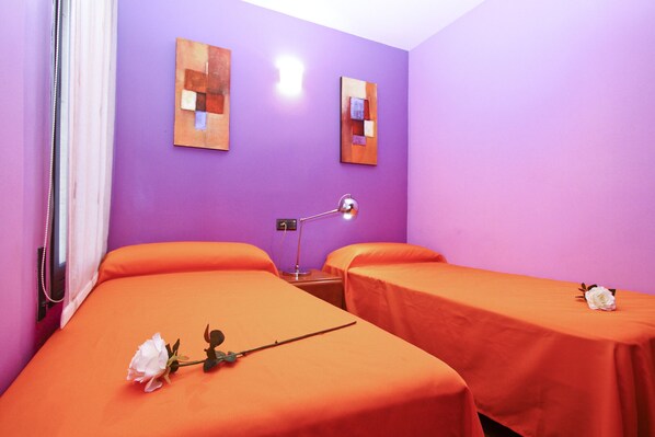 A room with two beds, a nightstand, a lamp, and artwork on the walls.