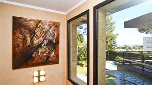 Een modern interieur met een groot abstract schilderij, een glazen deur naar een buitenzwembad en een zichtbaar stadsbeeld op de achtergrond.