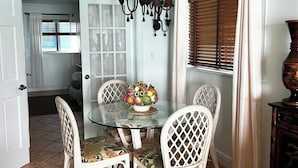 A dining area with a glass table surrounded by wicker chairs, a chandelier, and a vase with flowers. - Henry Louise & The Parrot (Moss Town)