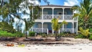 A beachfront property with a two-story building, a sandy beach, and clear turquoise waters. - Henry Louise & The Parrot (Moss Town)