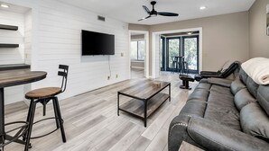 Un salon moderne doté d’un téléviseur à écran plat, d’un canapé, d’une table basse et d’un coin repas comprenant une chaise et une petite table.