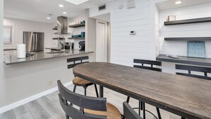 Une cuisine moderne dotée d’un îlot central, d’appareils électroménagers en acier inoxydable et d’un coin repas avec une longue table et des chaises en bois.