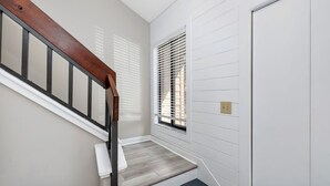 Un escalier avec une rampe en bois, un mur blanc orné d’une fenêtre et d’une porte.