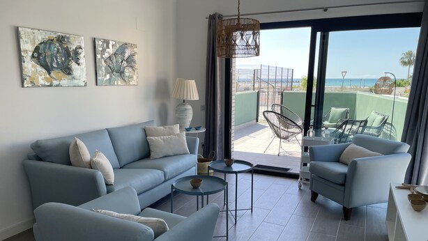 Un salon moderne avec un canapé bleu, des fauteuils, une table basse et une vue sur la mer grâce à de grandes portes vitrées.
