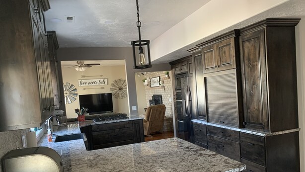 A modern kitchen with dark wood cabinets, a granite island, stainless steel appliances, and a ceiling fan. - Nice secluded home with plenty of room to roam! (Kanab)