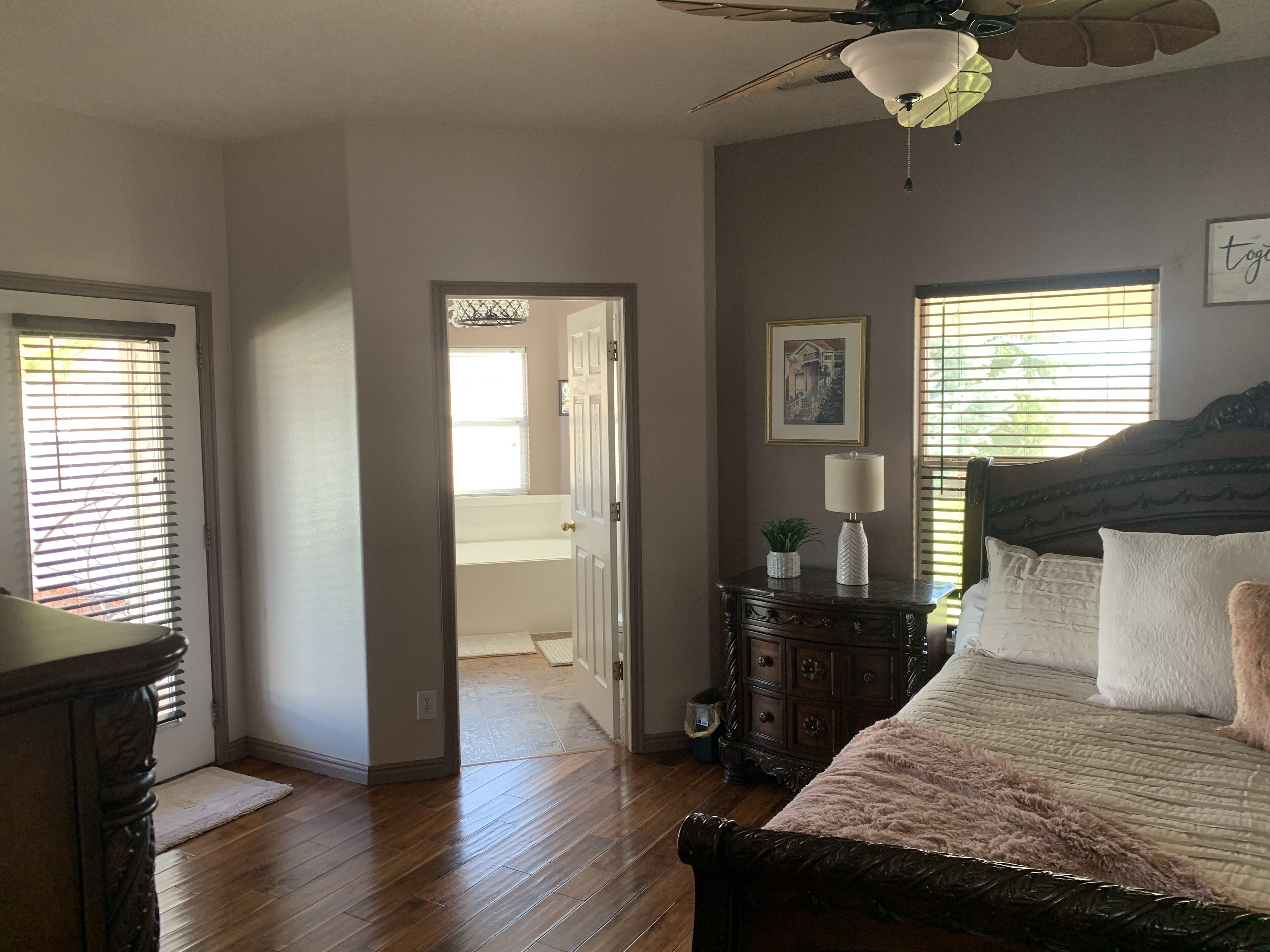 Une chambre à coucher comprenant un lit, une commode, un ventilateur de plafond et une fenêtre avec des stores.