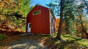 A red wooden building in a forested area with a gravel path leading to it. - Beautiful home located in the Mad River Valley (Warren)