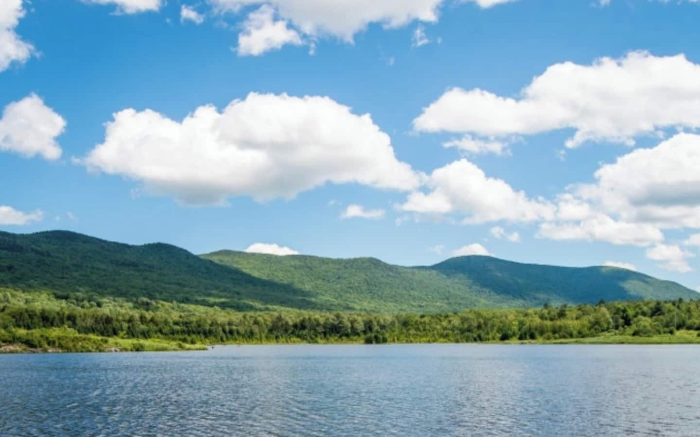 Ein See, umgeben von grünen Hügeln, unter blauem Himmel.