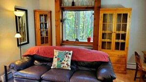 A cozy room with a leather sofa, a wooden cabinet, and a window with a view of trees. - Beautiful home located in the Mad River Valley (Warren)