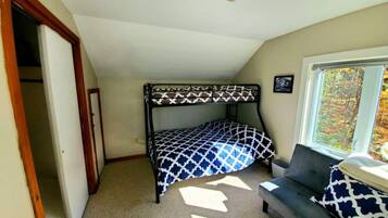 A room with a bunk bed, a sofa, a window with a view of trees, and a door leading to another room.