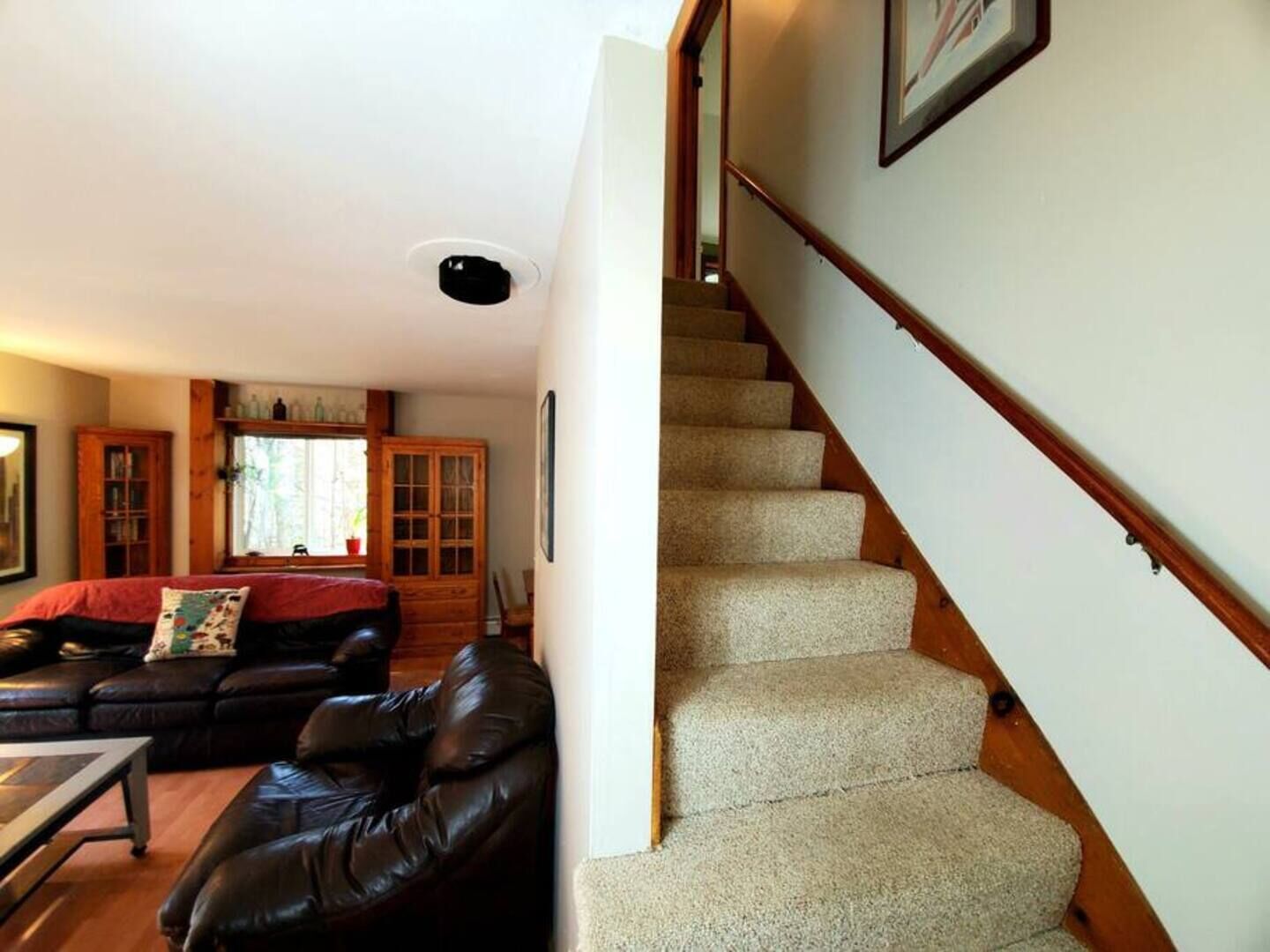 A living room with a leather sofa, a wooden cabinet, and a staircase with carpeted steps.