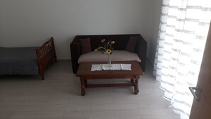 Une pièce comprenant un lit, un canapé, une table en bois recouverte d’une nappe en dentelle et un vase rempli de fleurs.