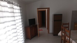 Une pièce comprenant un téléviseur posé sur un meuble en bois, un lit recouvert d’une couvre-lit à motifs floraux, une chaise en bois et une armoire.