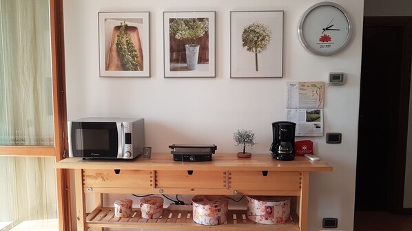 Uma bancada de cozinha com micro-ondas, cafeteira e uma pequena planta. Há quadros nas paredes acima da bancada.