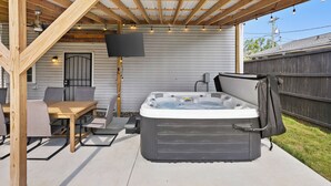 A covered outdoor patio with a hot tub, seating area, and a flat-screen TV.
