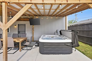 A covered outdoor patio with a hot tub, seating area, and a flat-screen TV.