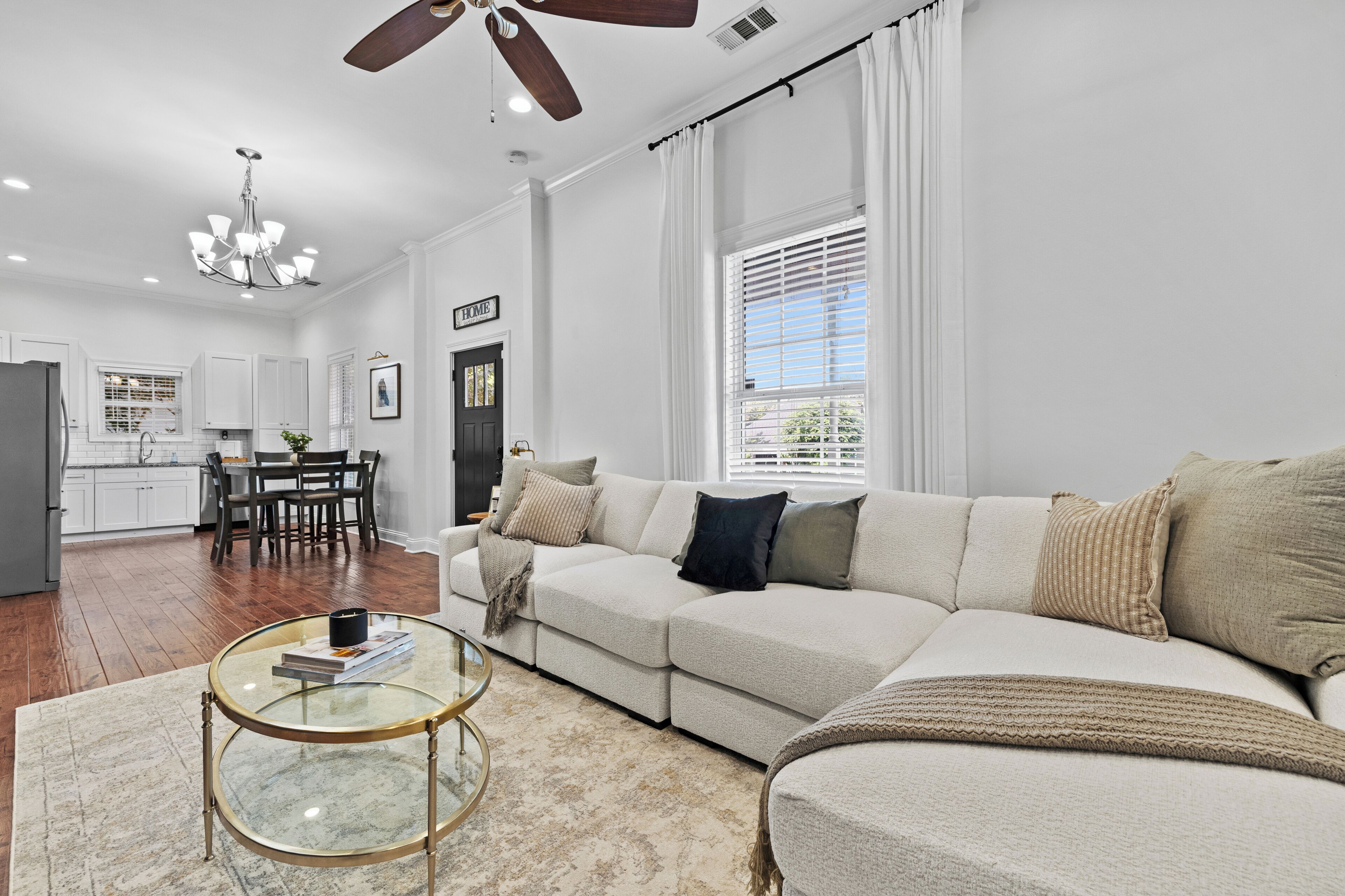 A spacious living room with a large sectional sofa, a glass coffee table, and a dining area with a kitchen in the background.