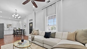 A spacious living room with a large sectional sofa, a glass coffee table, and a dining area with a kitchen in the background.