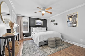 Ein Schlafzimmer mit einem Bett, Nachttischen, einem Deckenventilator, einem Fenster mit Vorhängen, einem Teppich und einem an der Wand befestigten Regal.