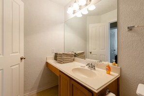A bathroom with a white sink, wooden cabinets, a mirror with lights, and a towel stack.