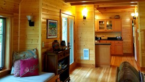 A cozy cabin interior with a wooden ceiling, a bed with pillows, a small table with a vase, and a kitchen area with cabinets and a refrigerator. - The "Belknap Cabin" (Blue River)