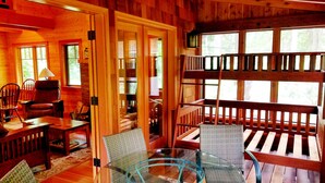 A wooden cabin interior with a glass table, wicker chairs, a wooden bench, and a staircase leading to a loft area. - The "Belknap Cabin" (Blue River)
