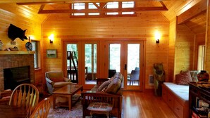 A cozy log cabin interior with a fireplace, wooden furniture, and a large window overlooking a forest. - The "Belknap Cabin" (Blue River)