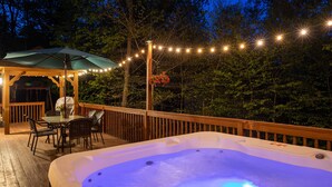 A hot tub on a wooden deck with string lights, surrounded by trees. - Hot Tub, Pool, Game Room and more fun for the whole family (East Stroudsburg)