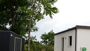 Un bâtiment moderne aux façades noire et blanche, entouré d’arbres et bordé d’une allée gravillonnée.