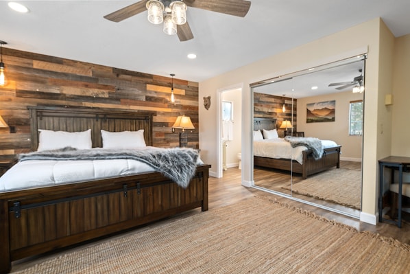 A bedroom with a wooden headboard, a large mirror, and a ceiling fan.