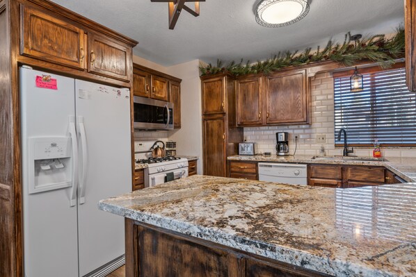 A kitchen with wooden cabinets, a white refrigerator, a microwave, a stove, and a granite countertop.