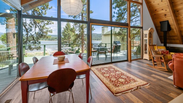 Una habitación amplia con una gran mesa de comedor de madera, sillas rojas y vistas a un lago a través de amplios ventanales.