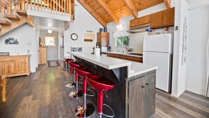 Una cocina amplia con vigas de madera, una isla central con taburetes rojos y un refrigerador blanco.