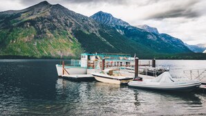 A docked boat with a cabin and a small boat in a lake with mountains in the background.