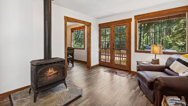 A cozy living room with a wood-burning stove, a leather sofa, and large windows offering a view of the outdoors.