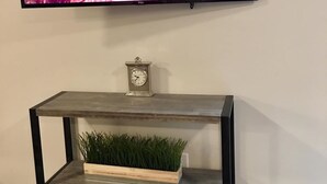 A flat-screen TV mounted on a wall above a wooden console table with a clock and a planter with green plants. - ❤️ 🏙 The View-Stylish Interior- Min to downtwn 🌃 ❤️ (Cincinnati)