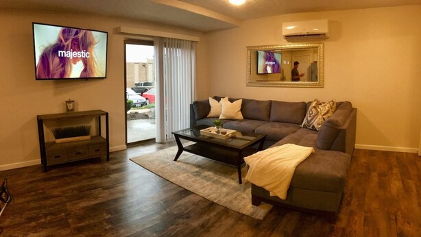 A living room with a dark brown sofa, a glass coffee table, and a television mounted on the wall. - ❤️ 🏙 The View-Stylish Interior- Min to downtwn 🌃 ❤️ (Cincinnati)