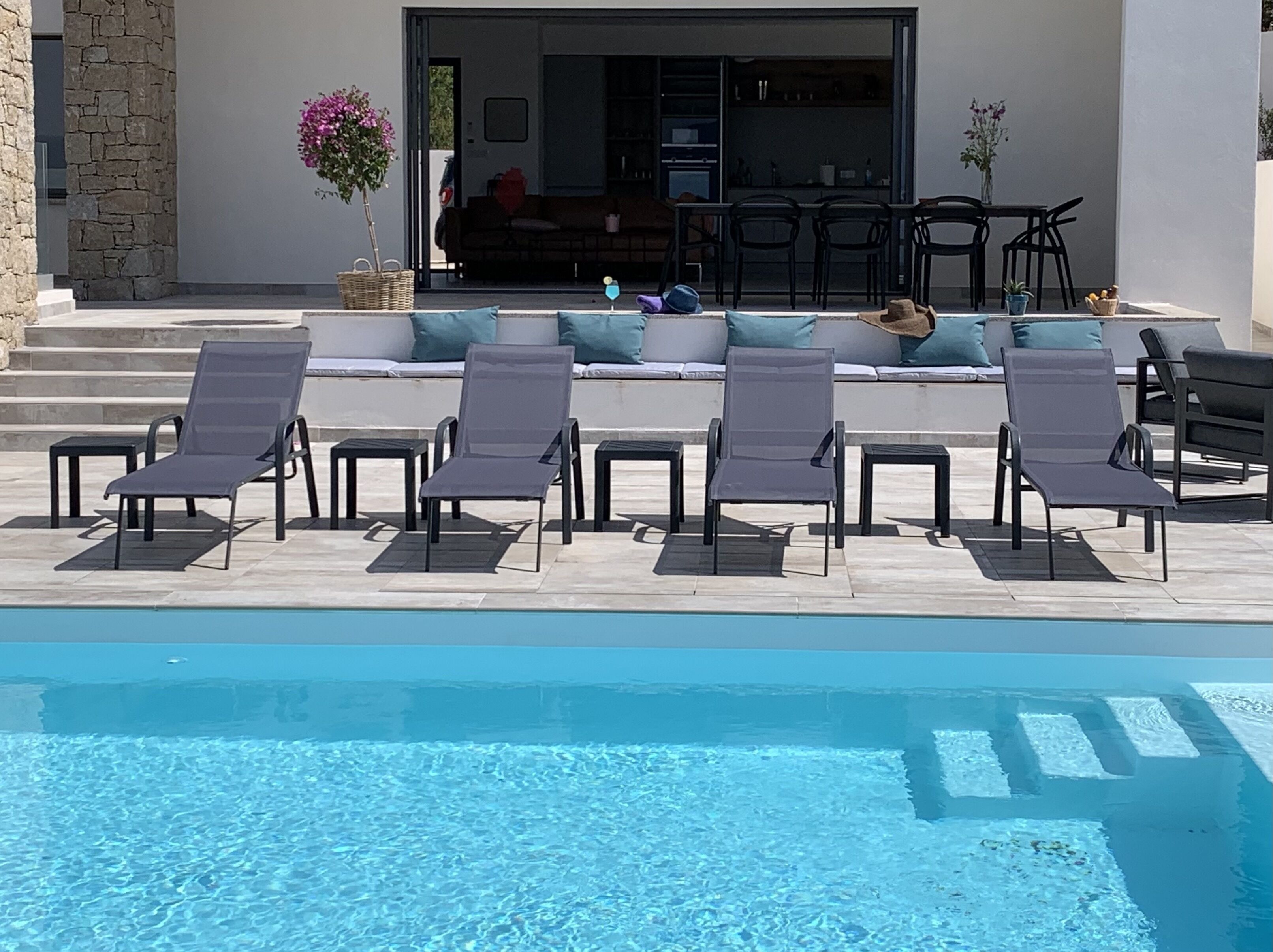 A poolside area with lounge chairs and a view of a modern interior with a sofa and dining area.