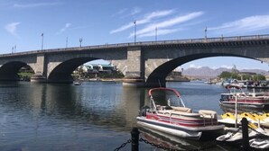 Eine Brücke mit drei Bögen über dem Wasser, Boote im Yachthafen vertäut, und Berge im Hintergrund.
