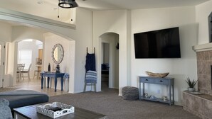 Ein geräumiges Wohnzimmer mit Deckenventilator, Kamin, Wand-Fernseher und Essbereich mit Stühlen und Tisch.